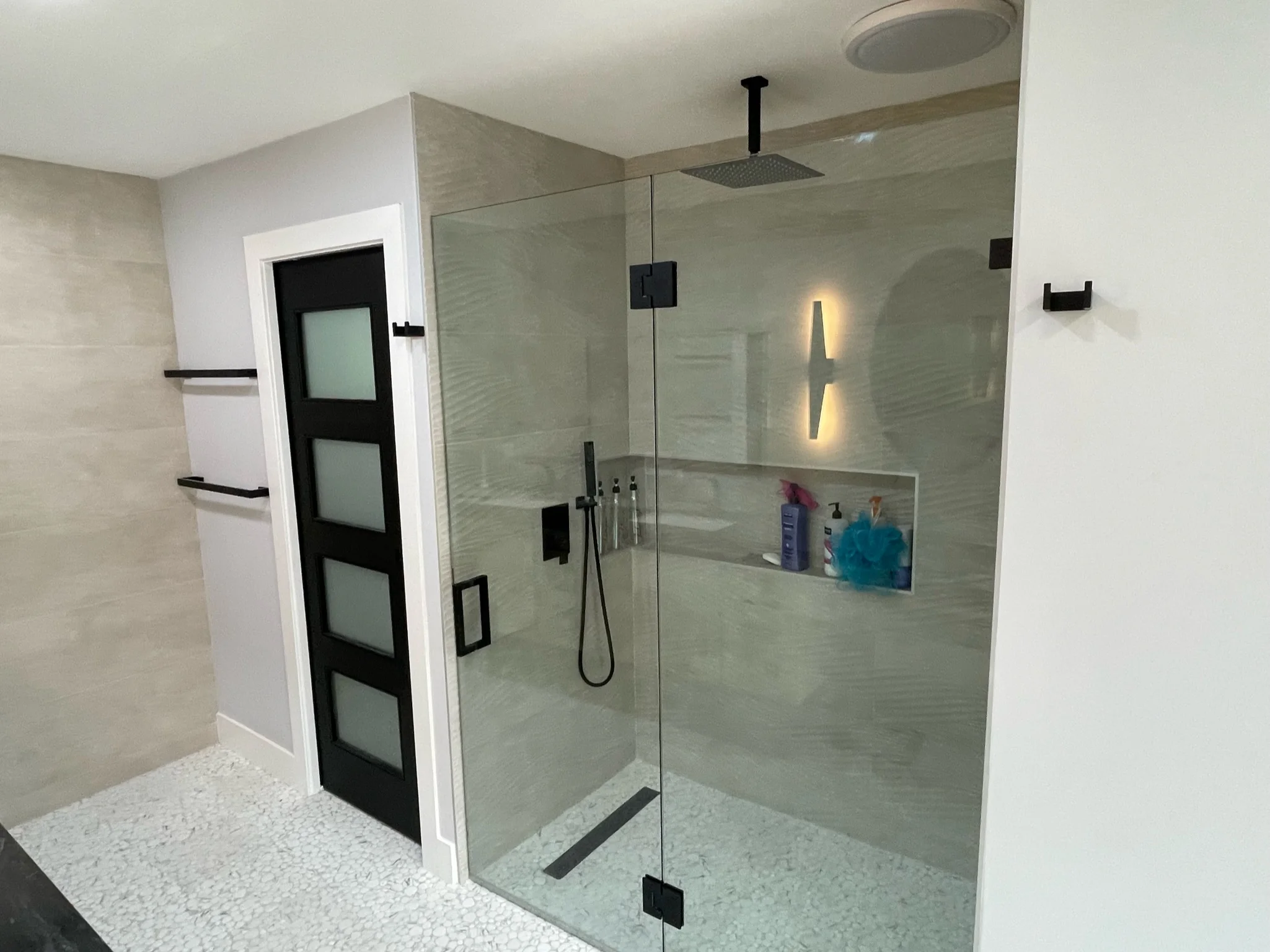 Modern bathroom with frameless glass shower, gray tile walls, and black fixtures
