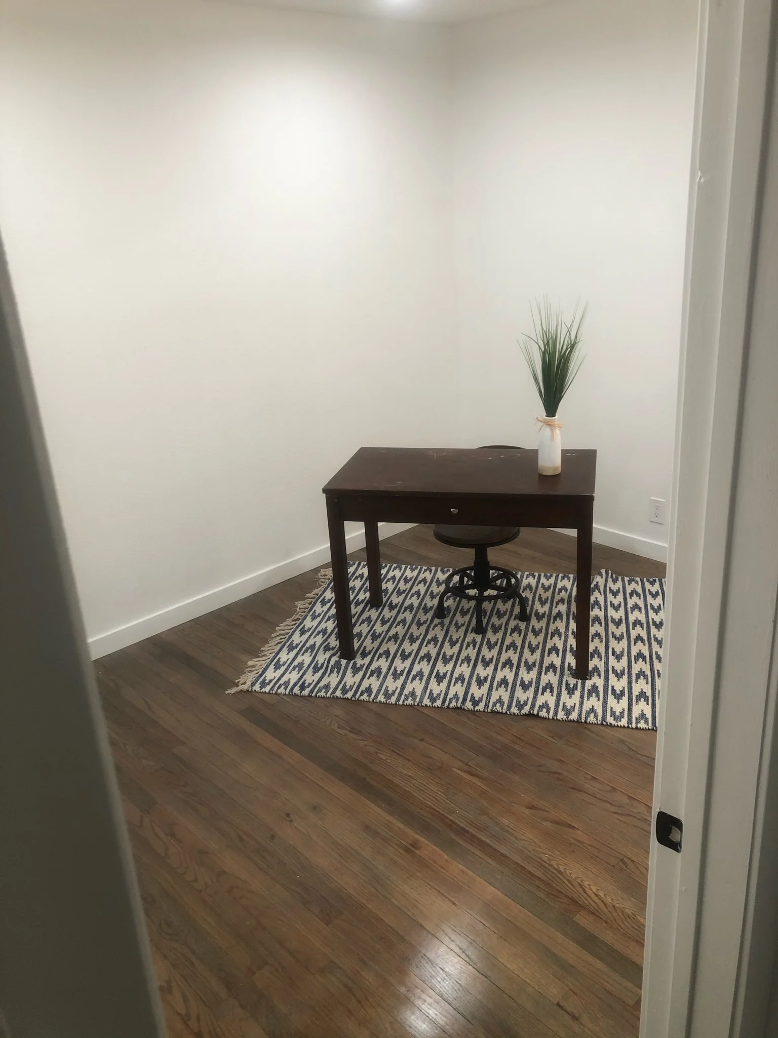 Modern office room with dark wood flooring, white walls, and contemporary desk setup