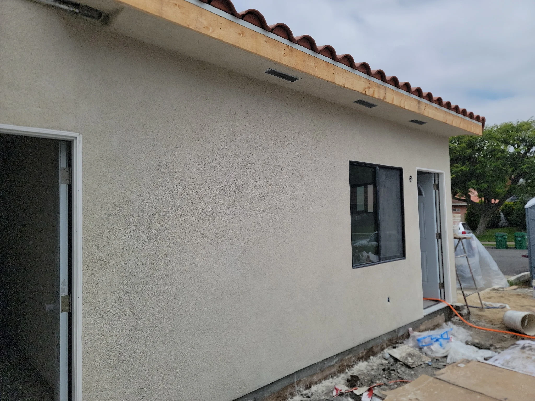New stucco addition with dark windows and clay tile roof during construction phase