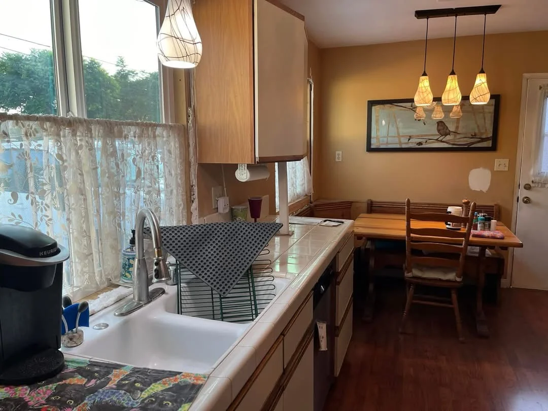 Renovated kitchen with golden walls, dark wood cabinets, and pendant lighting overlooking dining area