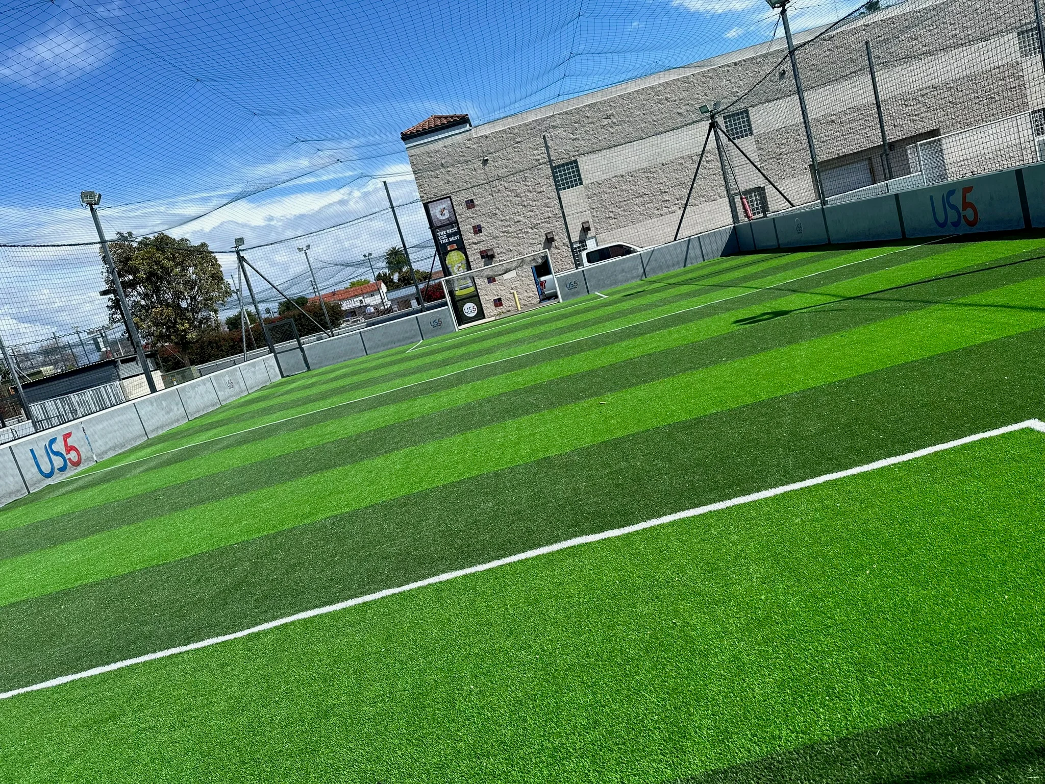 Newly installed synthetic turf soccer field with white lines, safety netting, and brick building backdrop