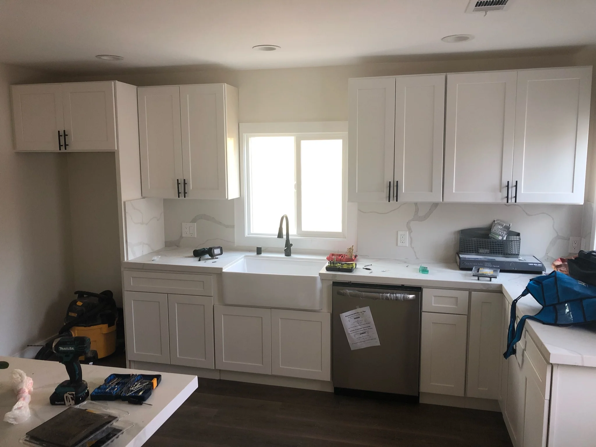 Modern kitchen with white cabinetry, white countertops, and marble backsplash during renovation