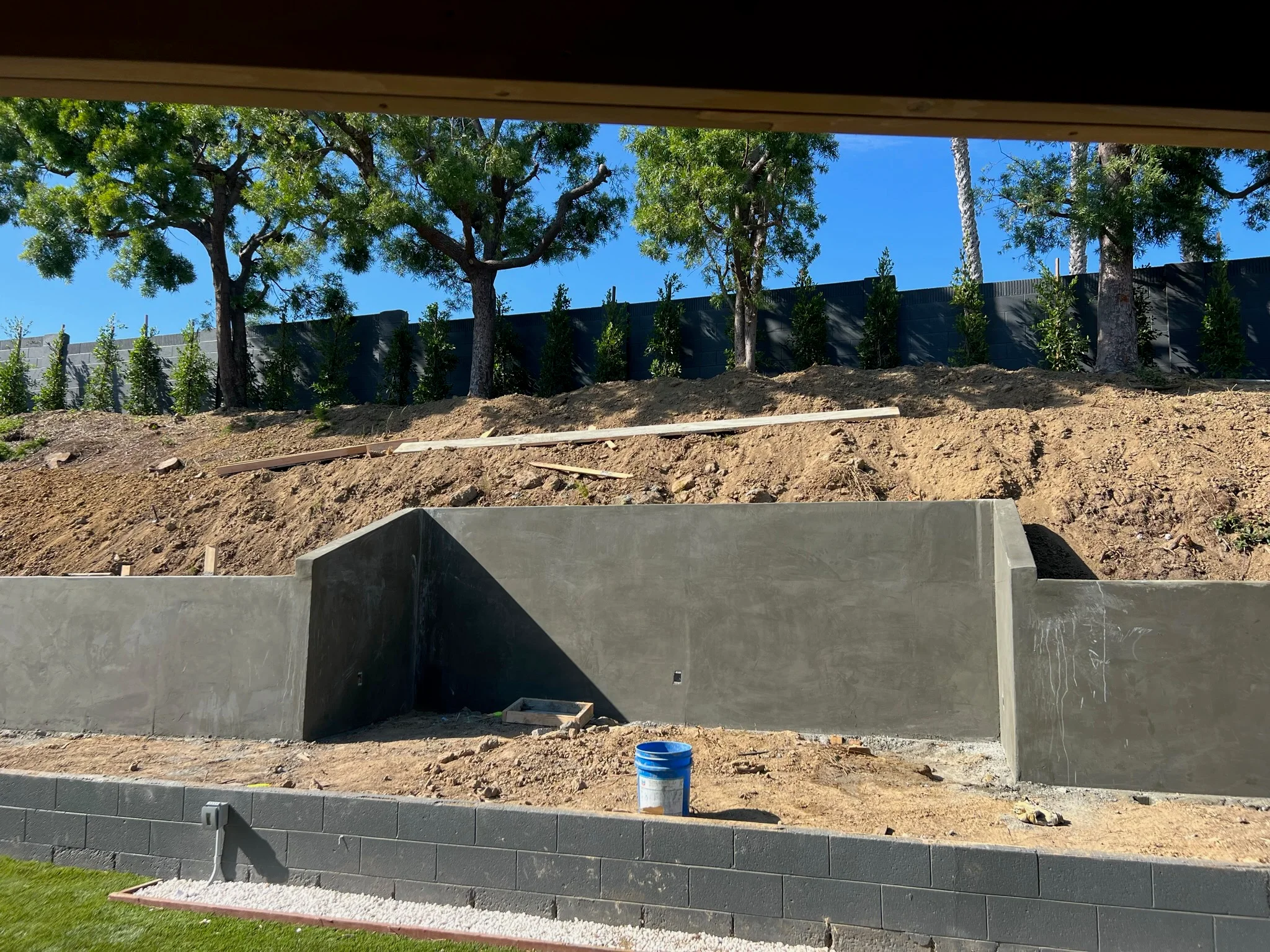 Concrete foundation and retaining wall under construction on sloped lot with mature trees