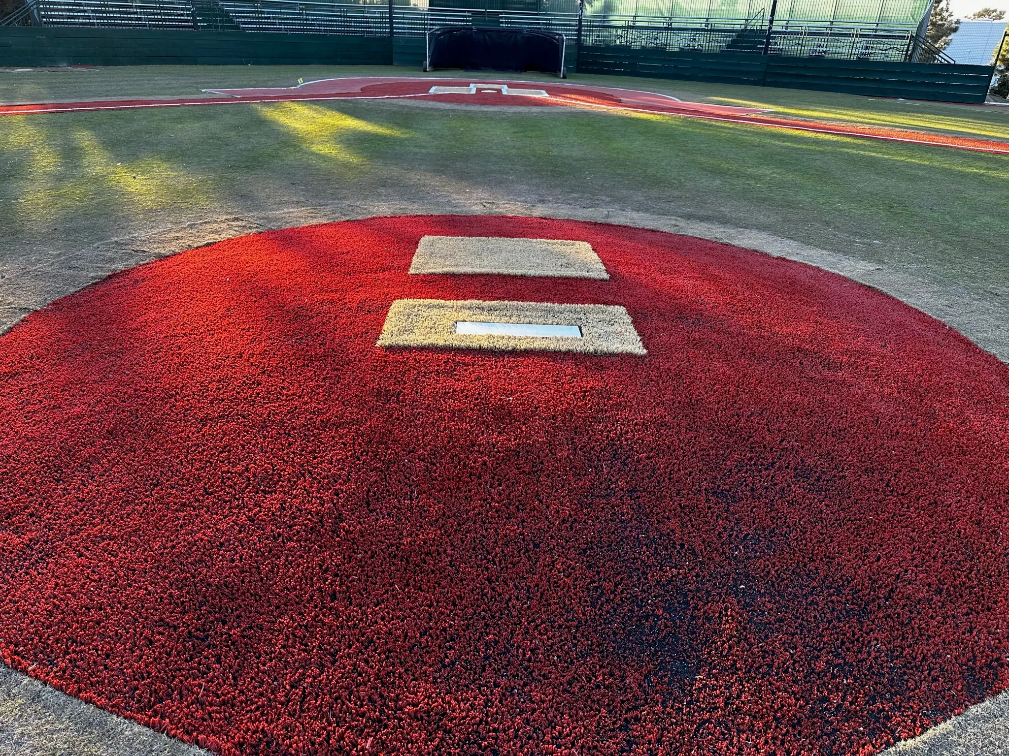 Red clay baseball infield with white base markers and pitcher's mound at sports facility