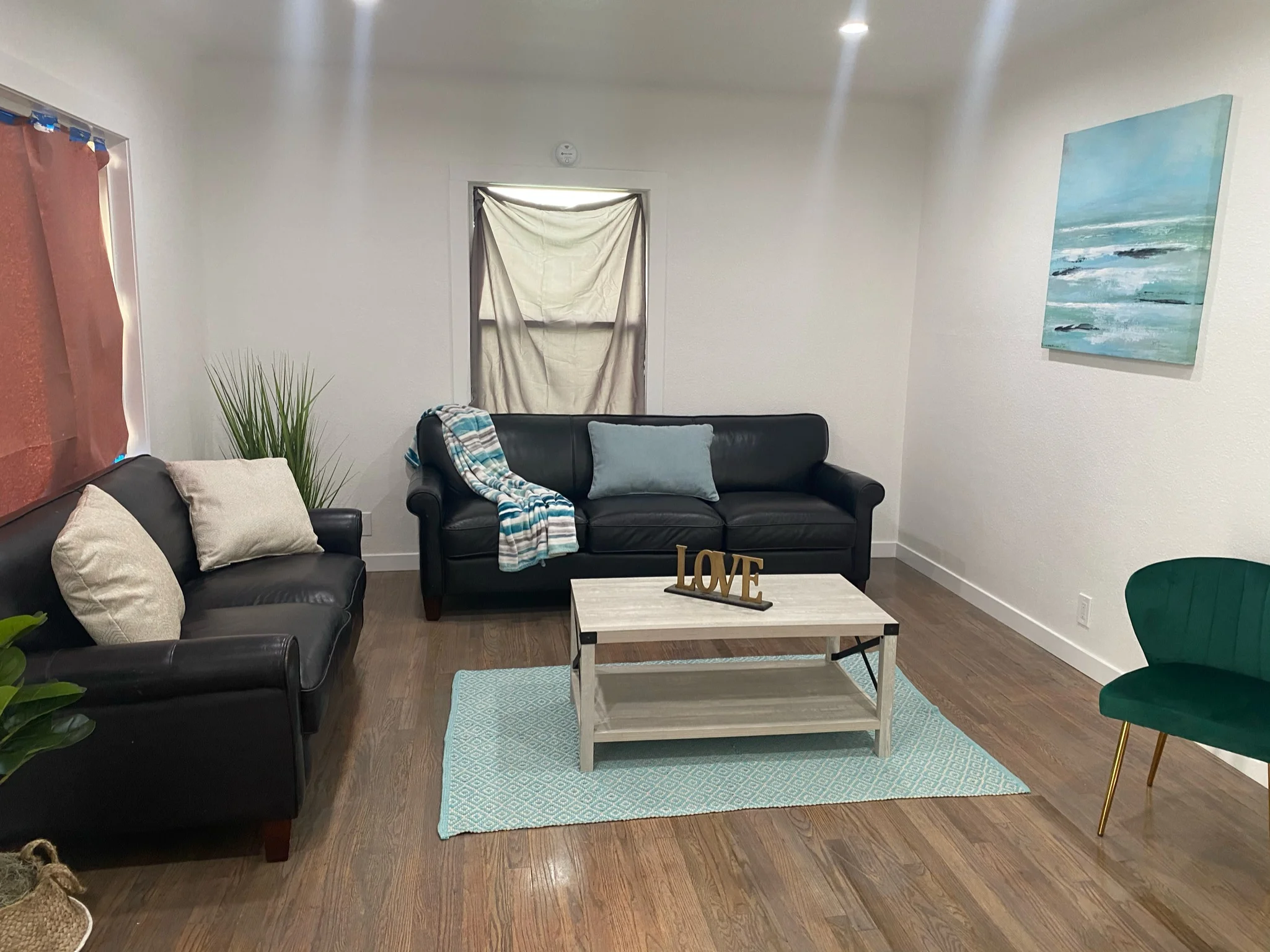 Renovated living room with black leather sofa, light wood coffee table, and hardwood flooring