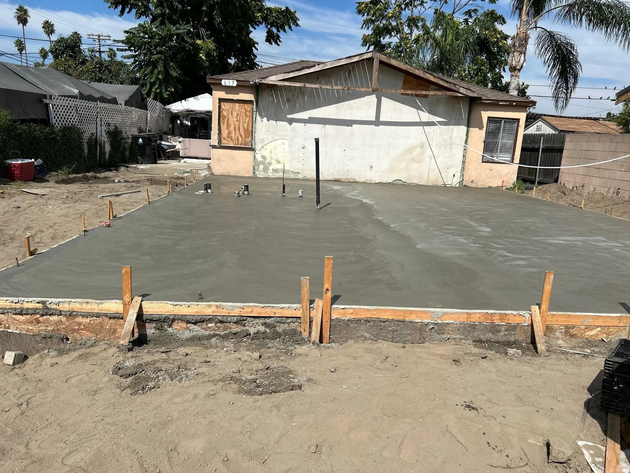 Newly poured concrete foundation slab with wooden forms and support posts in residential backyard