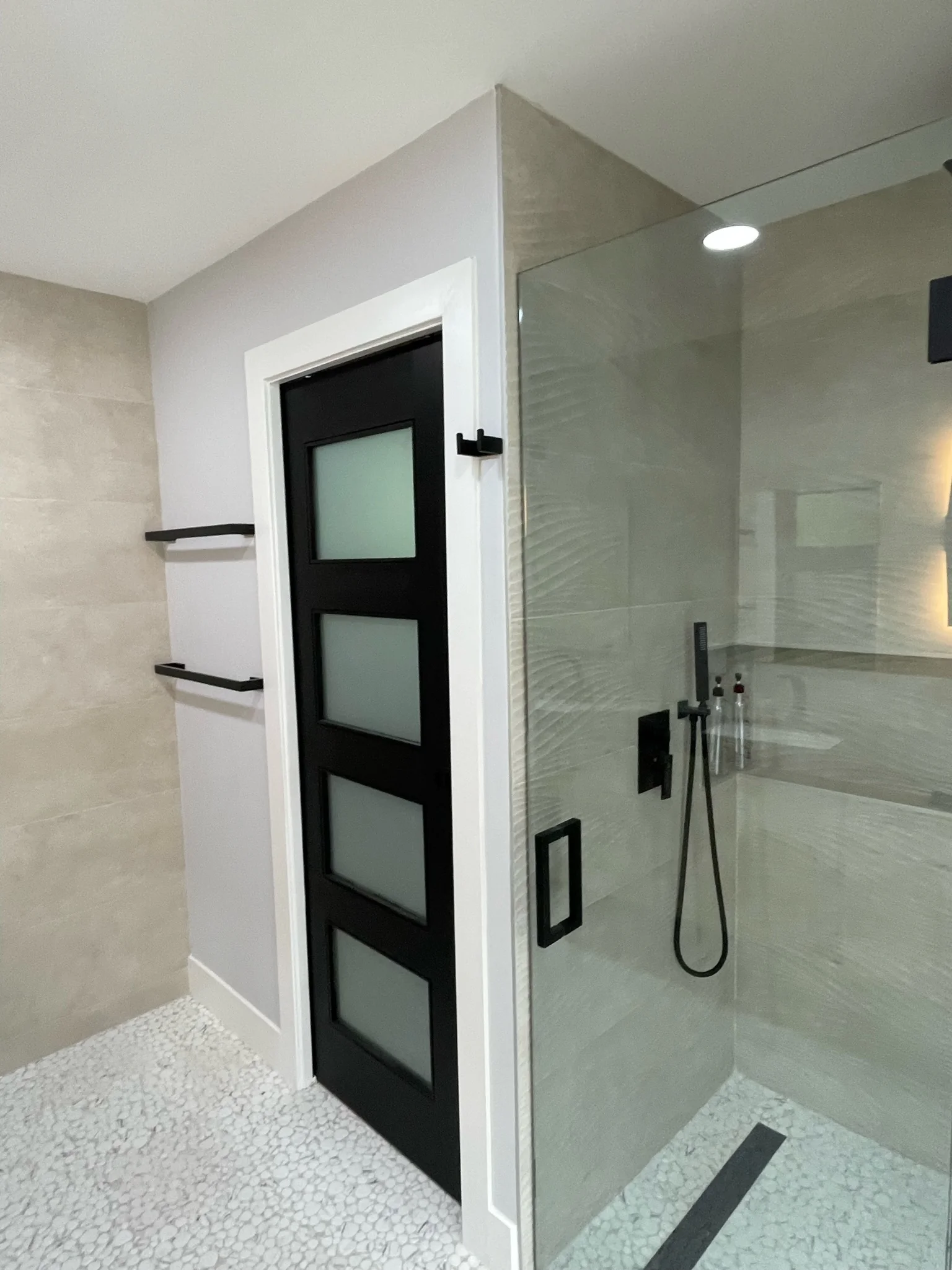 Modern bathroom with frameless glass shower enclosure, neutral tile walls, and black fixtures