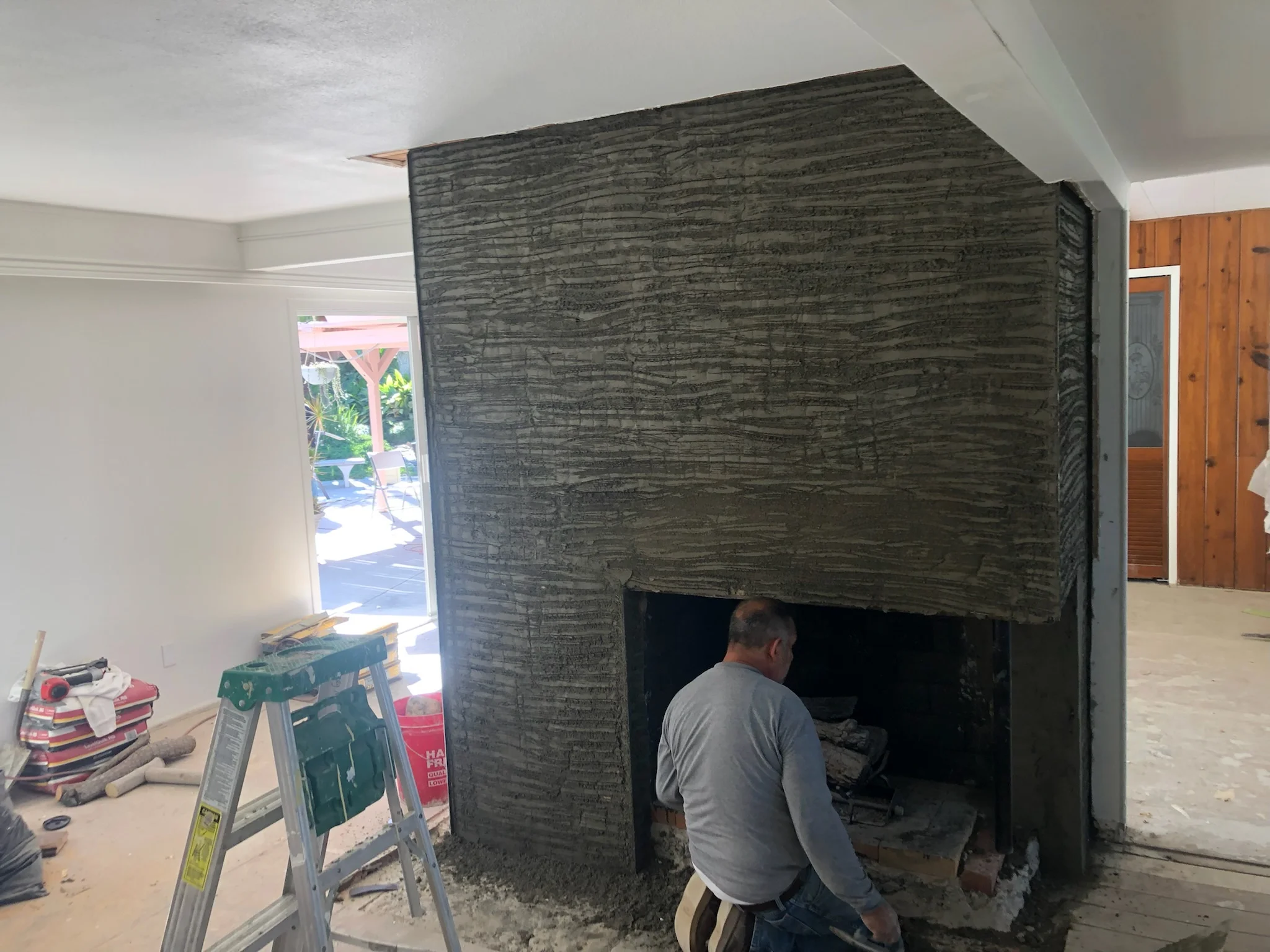 Worker installing dark brick fireplace surround with open hearth opening in residential interior