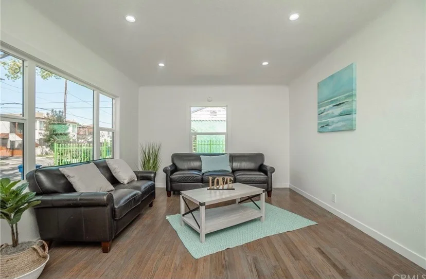 Bright modern living room with black leather furniture, hardwood floors, and large windows