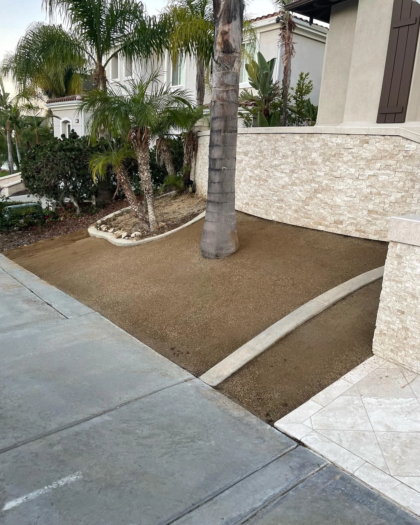 Decorative aggregate patio with concrete edging, palm trees, and stone veneer walls