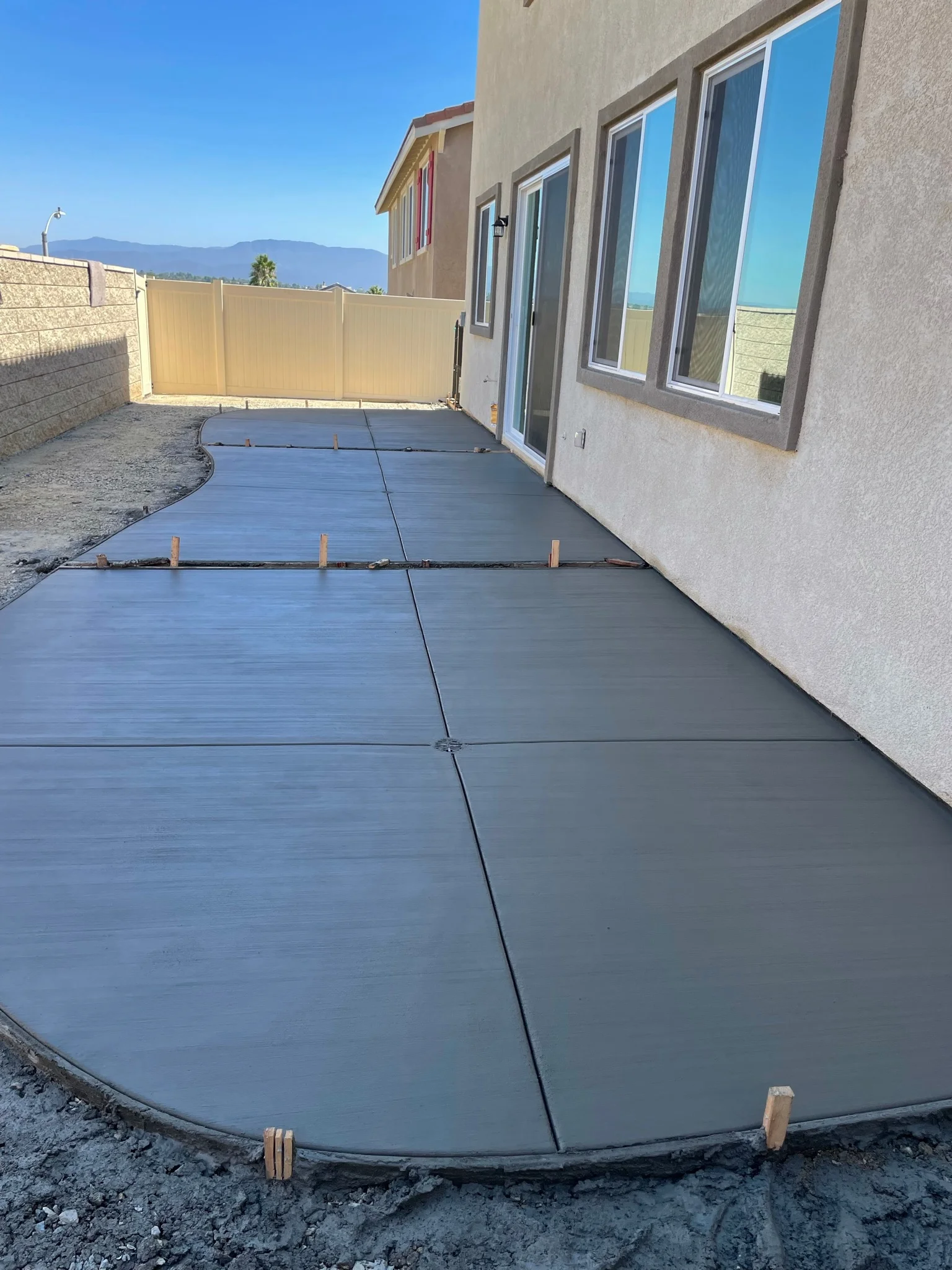 Newly poured concrete patio with control joints adjacent to residential home and retaining wall