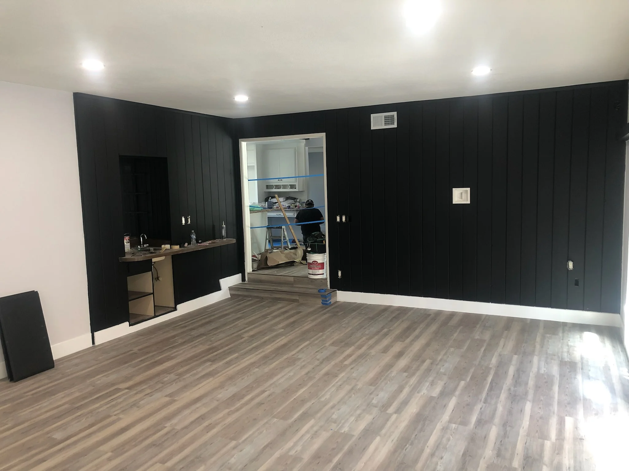 Modern commercial interior with black shiplap walls, gray vinyl plank flooring, and kitchenette