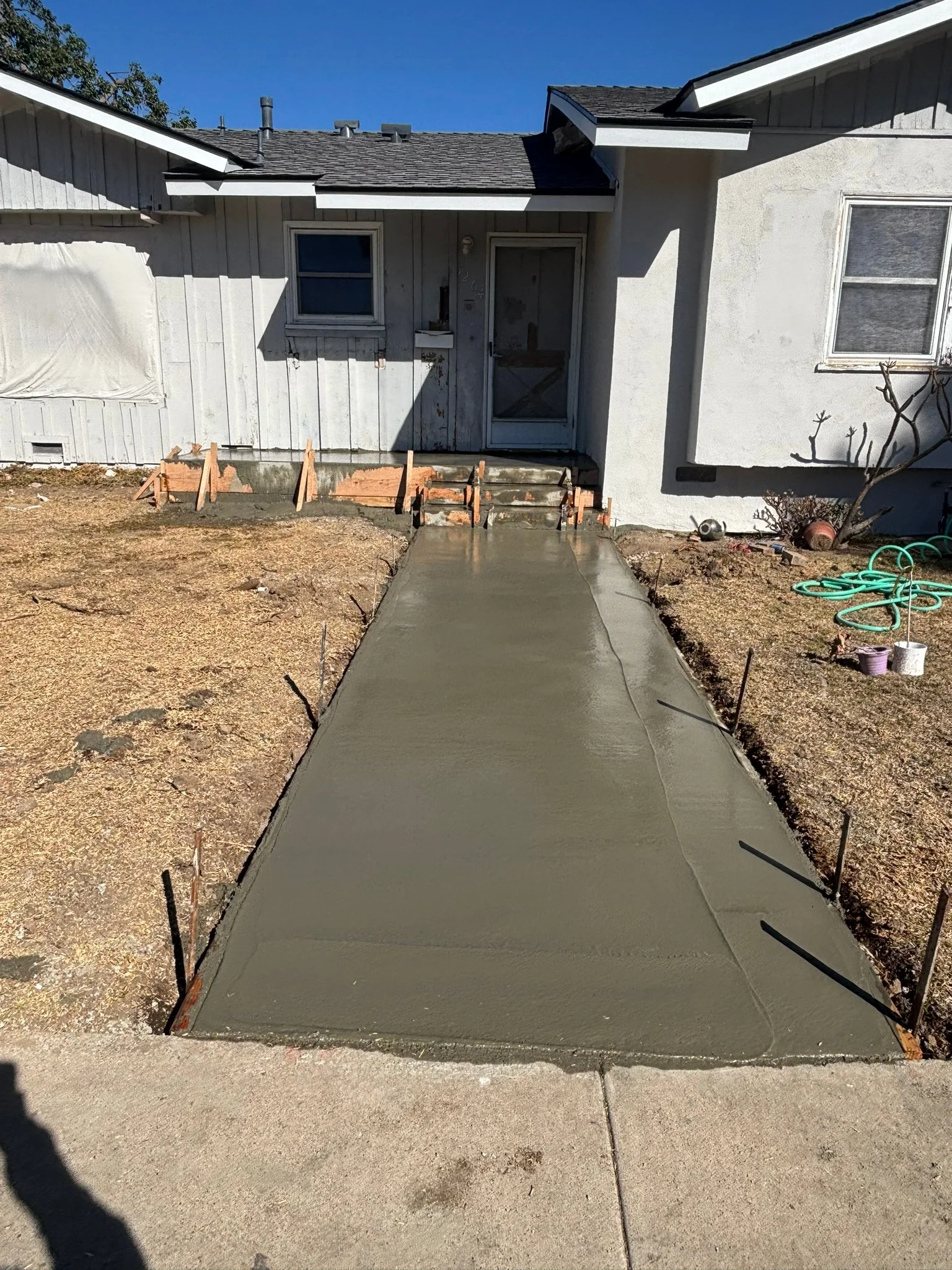 Freshly poured concrete walkway with wooden forms and rebar visible along residential home entrance