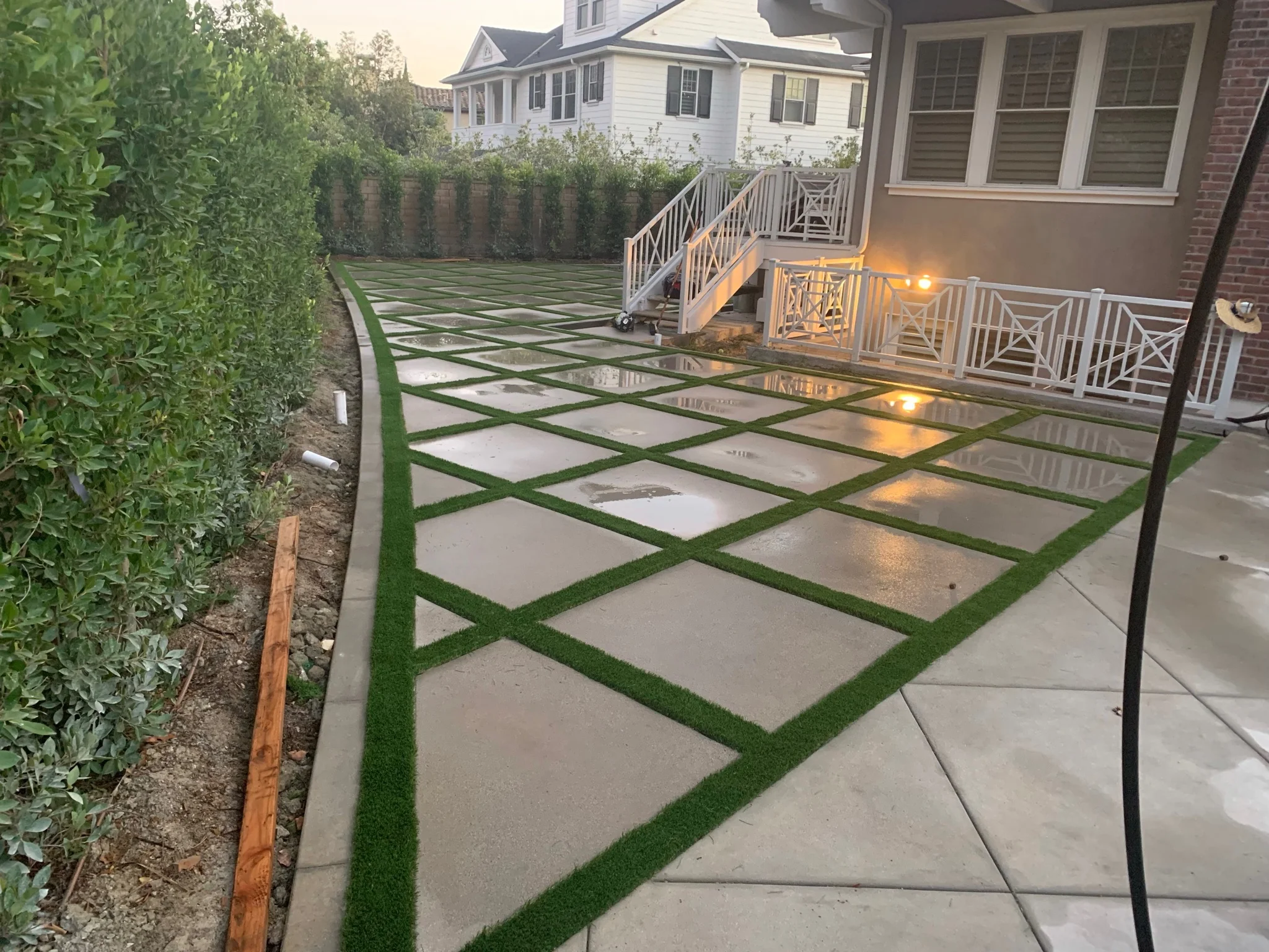 Geometric concrete patio with synthetic turf strips and landscape lighting at dusk