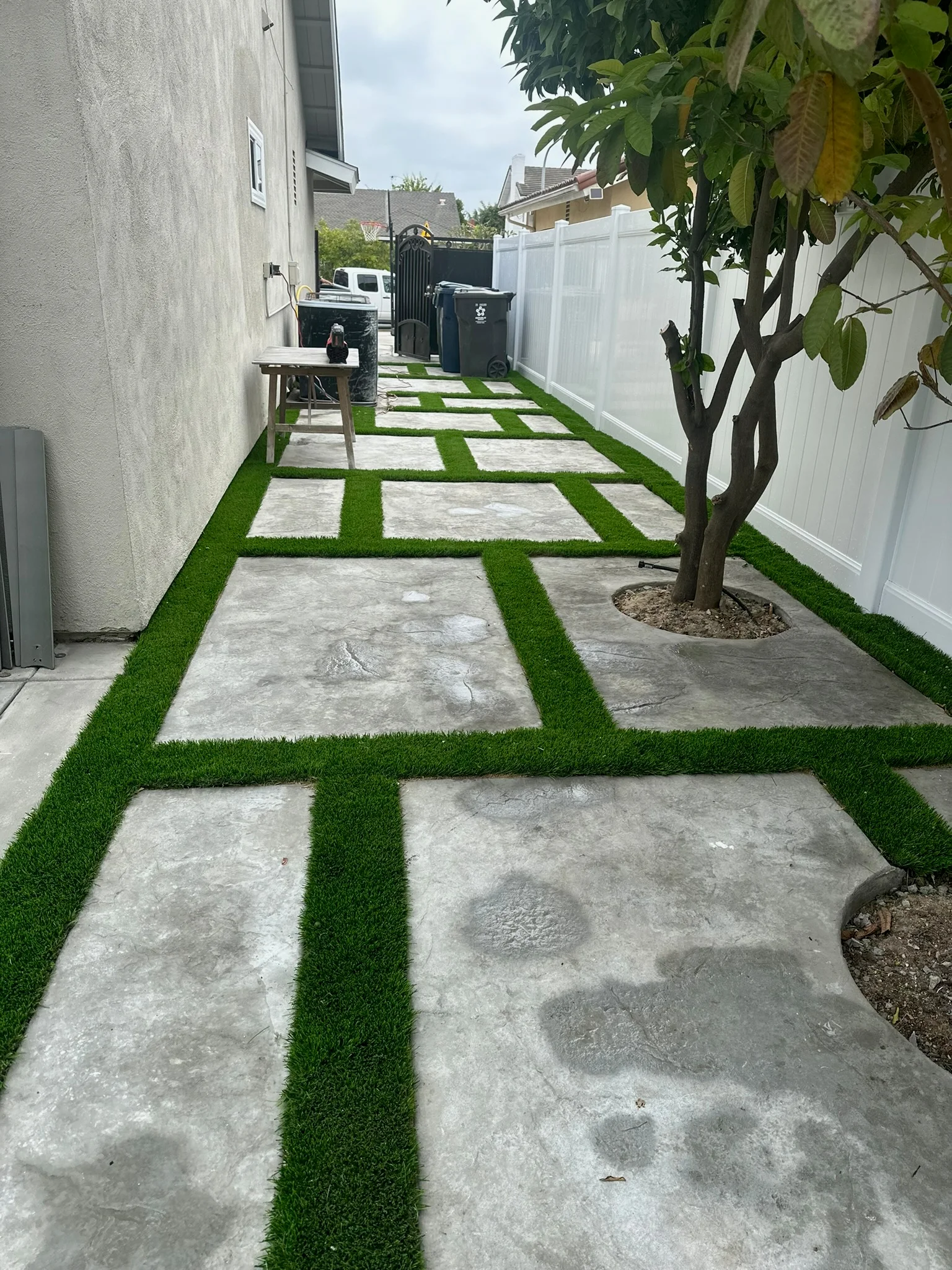 Side yard with concrete pavers and artificial turf strips creating geometric pattern