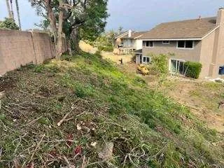 Cleared hillside lot with graded earth and removed vegetation near residential home