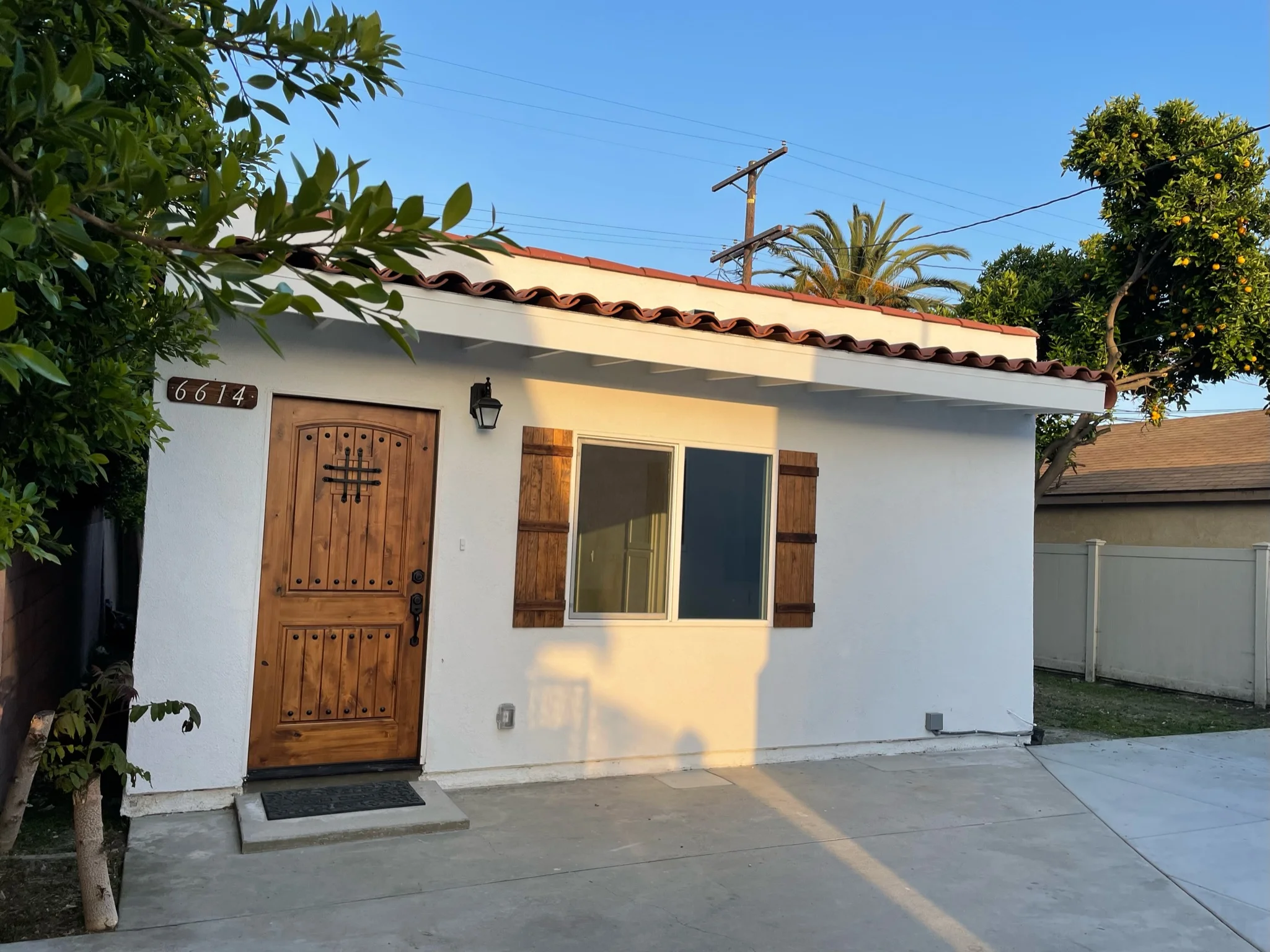 White stucco Spanish Colonial home with clay tile roof, wooden door, and shuttered windows