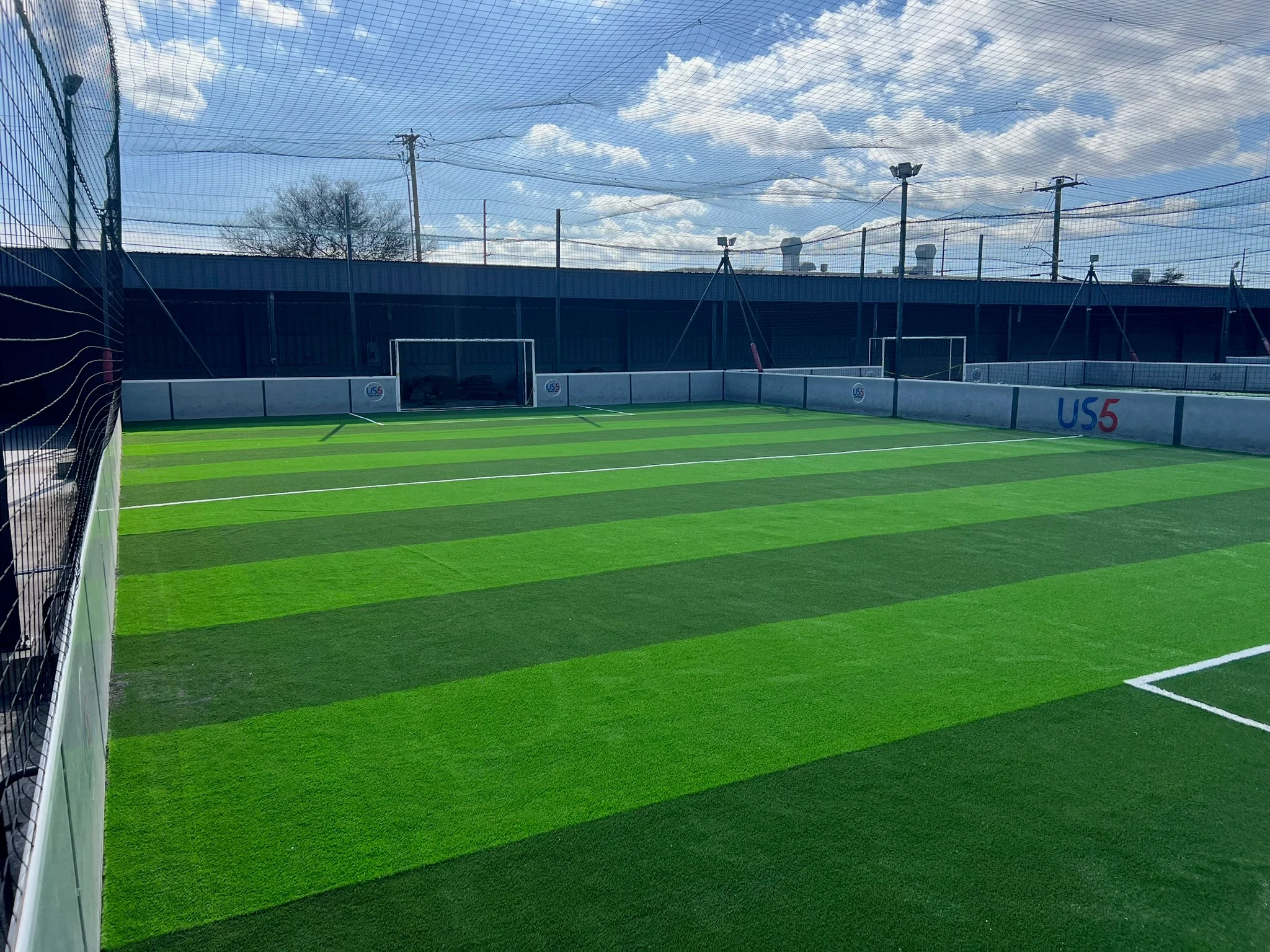 Indoor soccer field with bright green synthetic turf, white goal frames, and protective netting