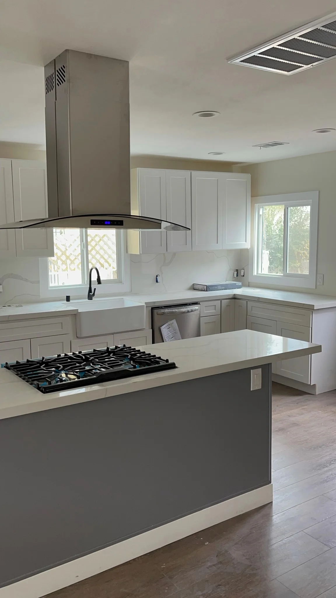 Modern kitchen with white cabinets, gray island, gas cooktop, and curved range hood