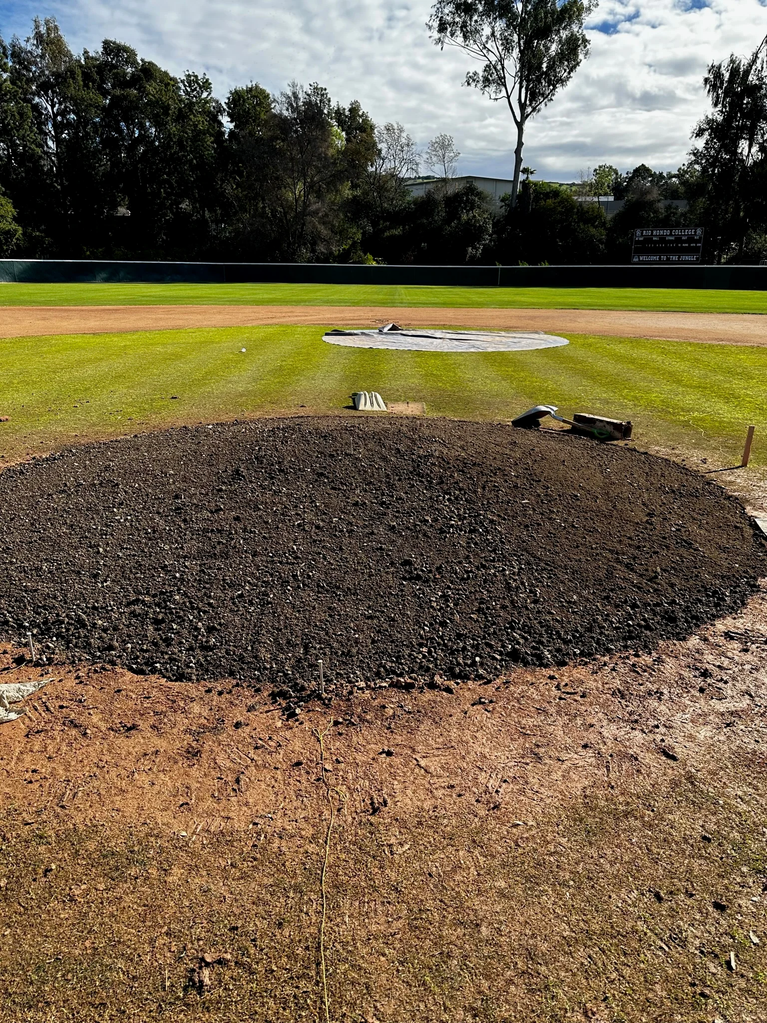 Baseball infield under construction with dark aggregate material and mound preparation visible
