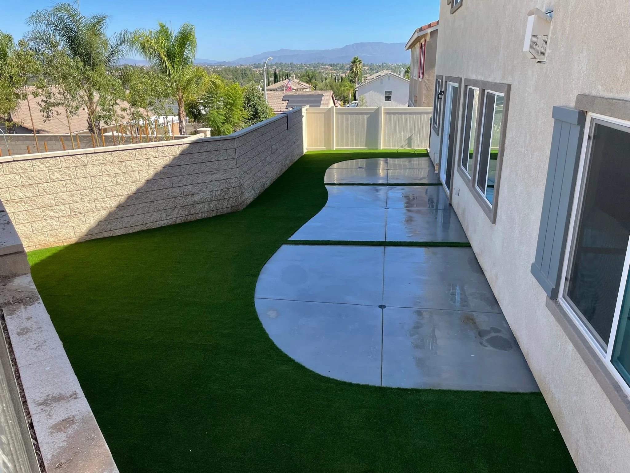 Backyard patio with polished concrete, synthetic turf, and retaining wall overlooking Riverside valley
