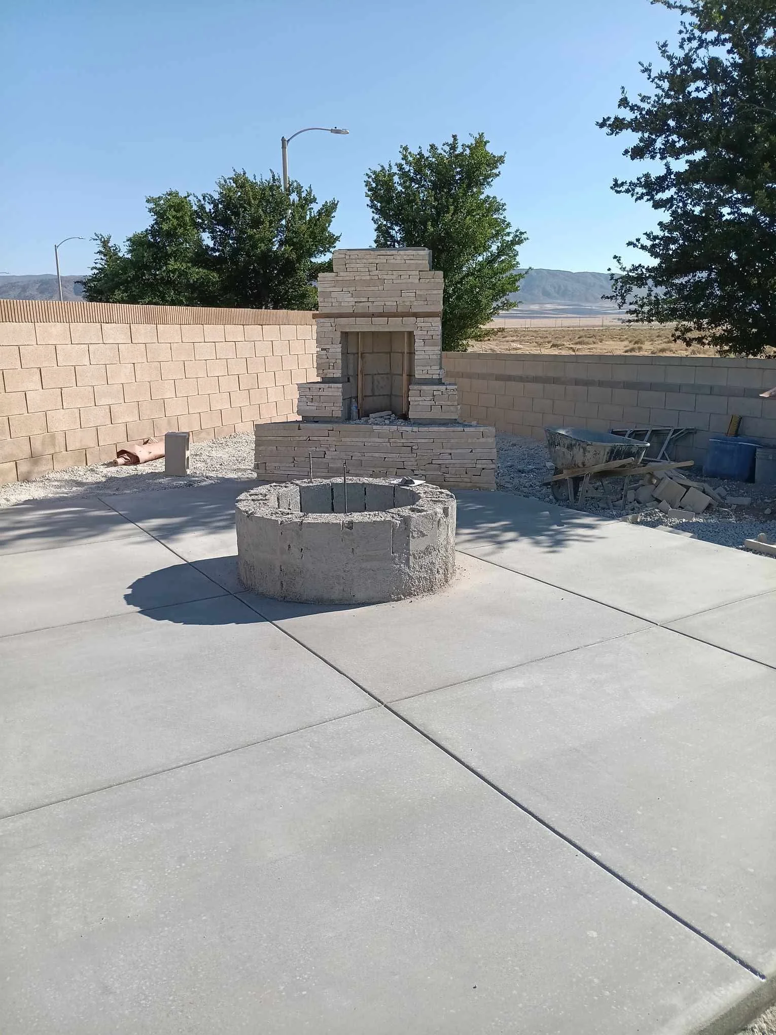 Concrete patio with circular fire pit and brick chimney structure in residential backyard