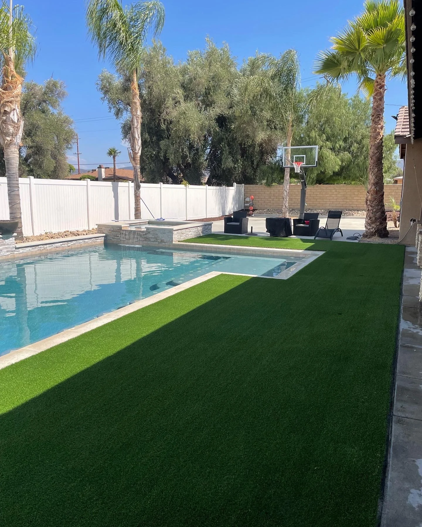 Completed backyard with pool, spa, synthetic turf, and palm trees under clear blue sky