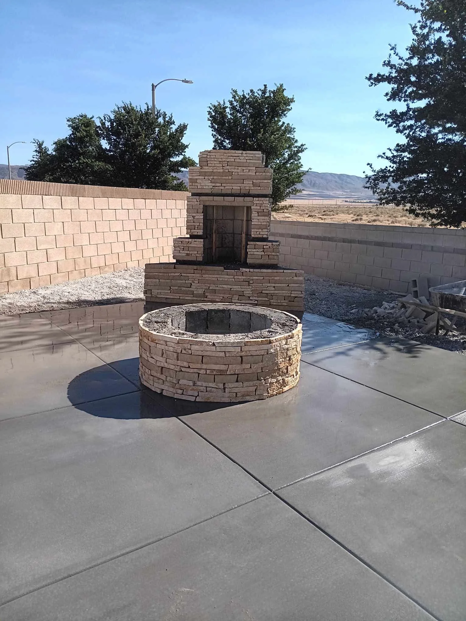 Circular stone fire pit on concrete patio with masonry chimney and block walls