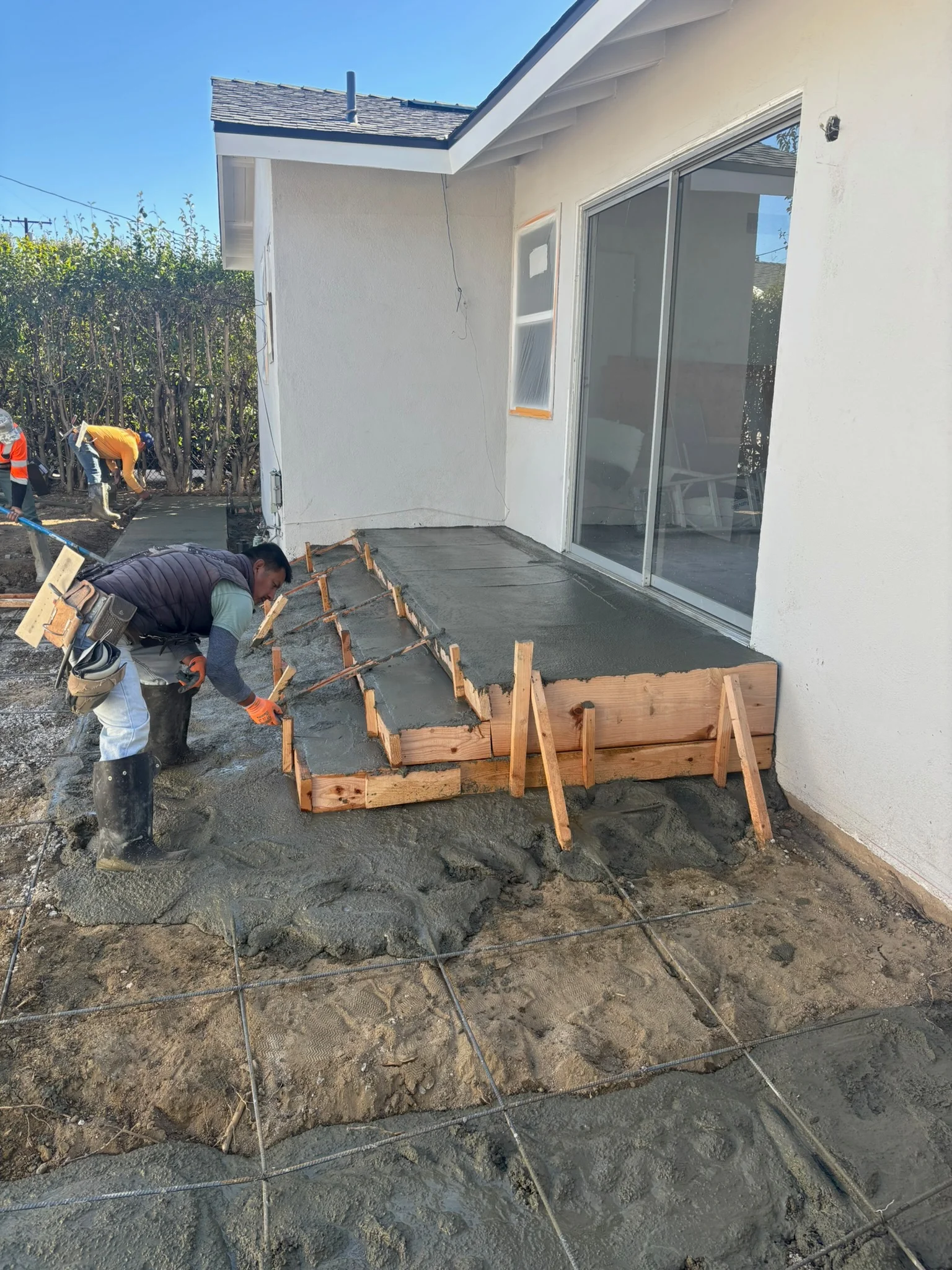 Concrete patio installation with wooden forms and workers finishing surface near modern home