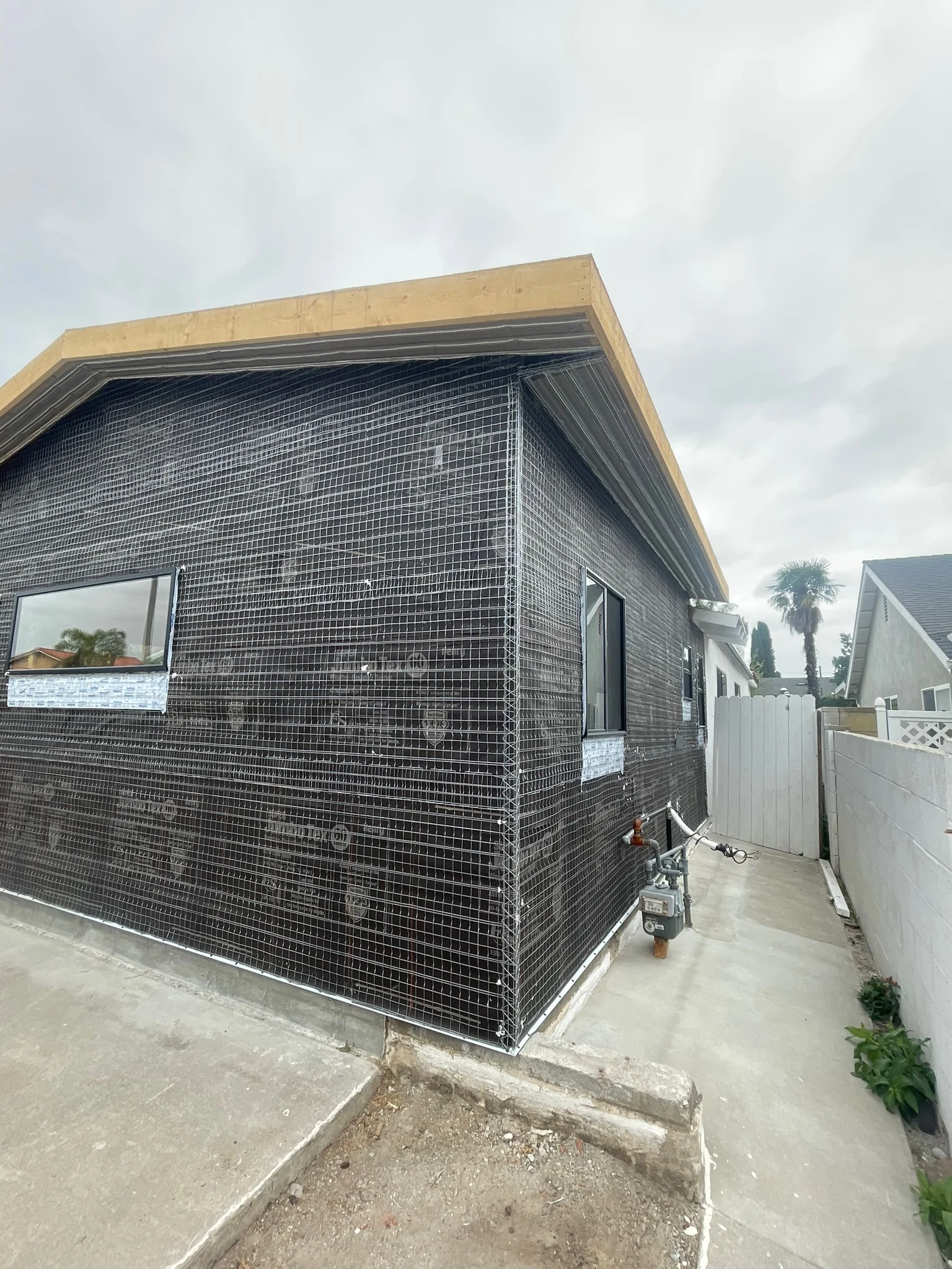 Modern home addition with dark metal mesh cladding, wood trim, and concrete foundation in Riverside