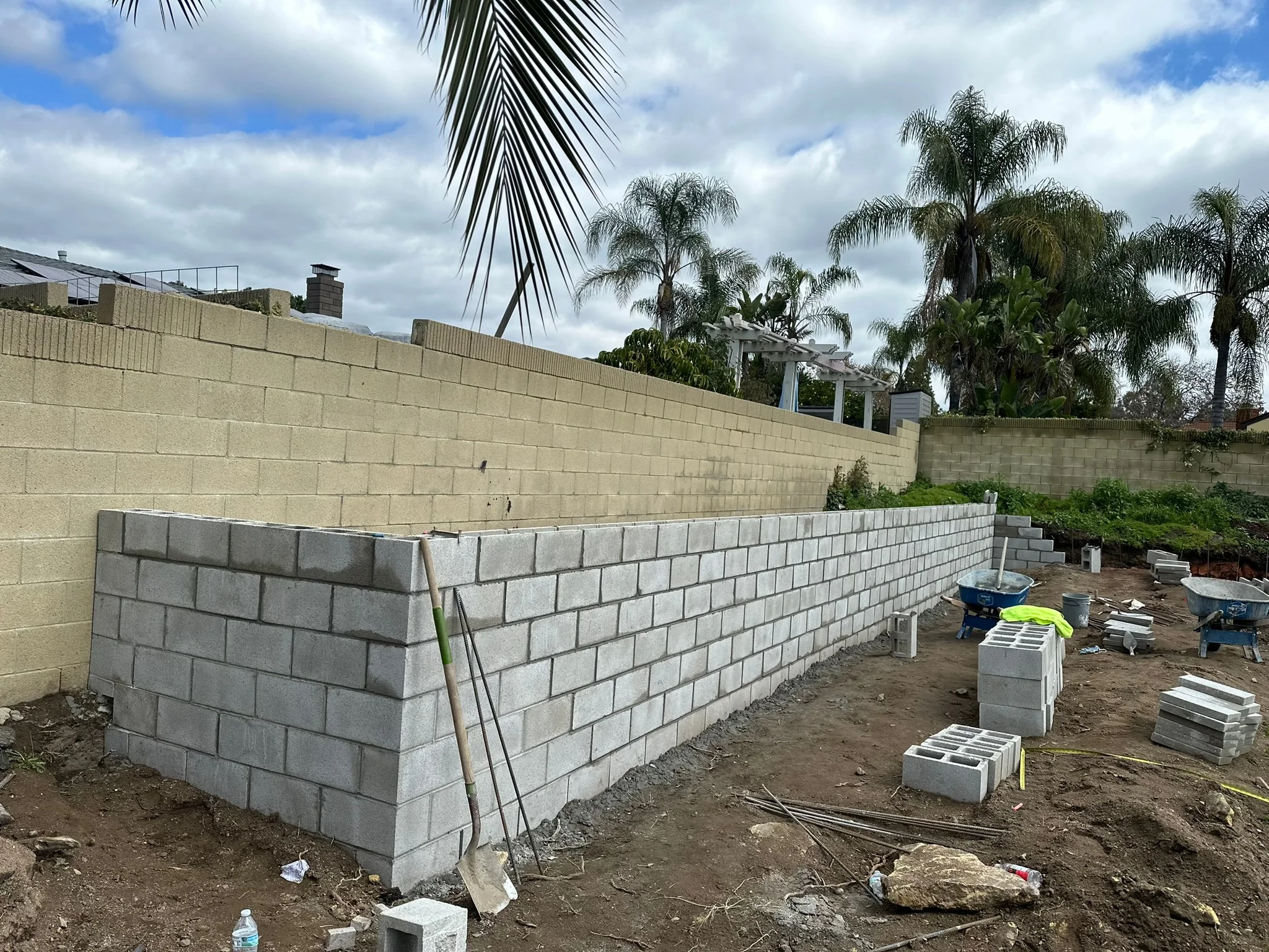 Concrete block retaining wall under construction with staged materials and equipment on site