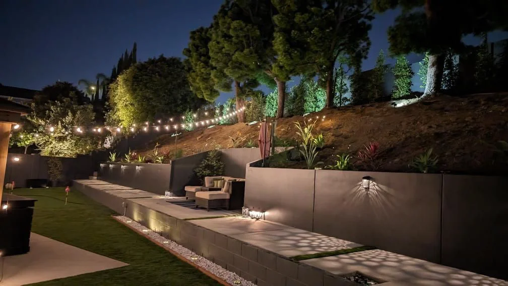 Illuminated modern hillside landscape with tiered concrete walls and planted terraces at dusk