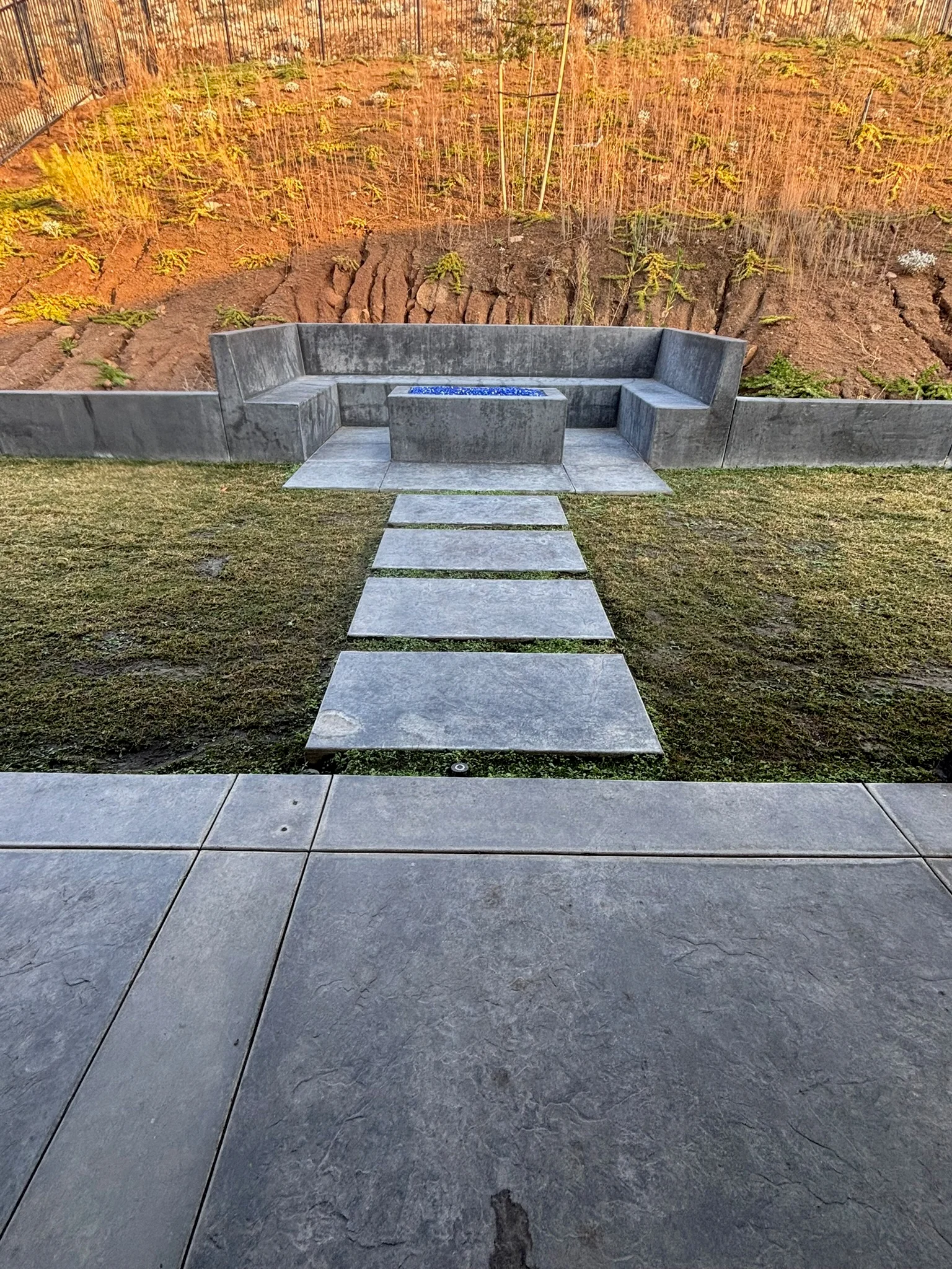 Concrete fire pit seating area with stepping stones and built-in benches in residential backyard