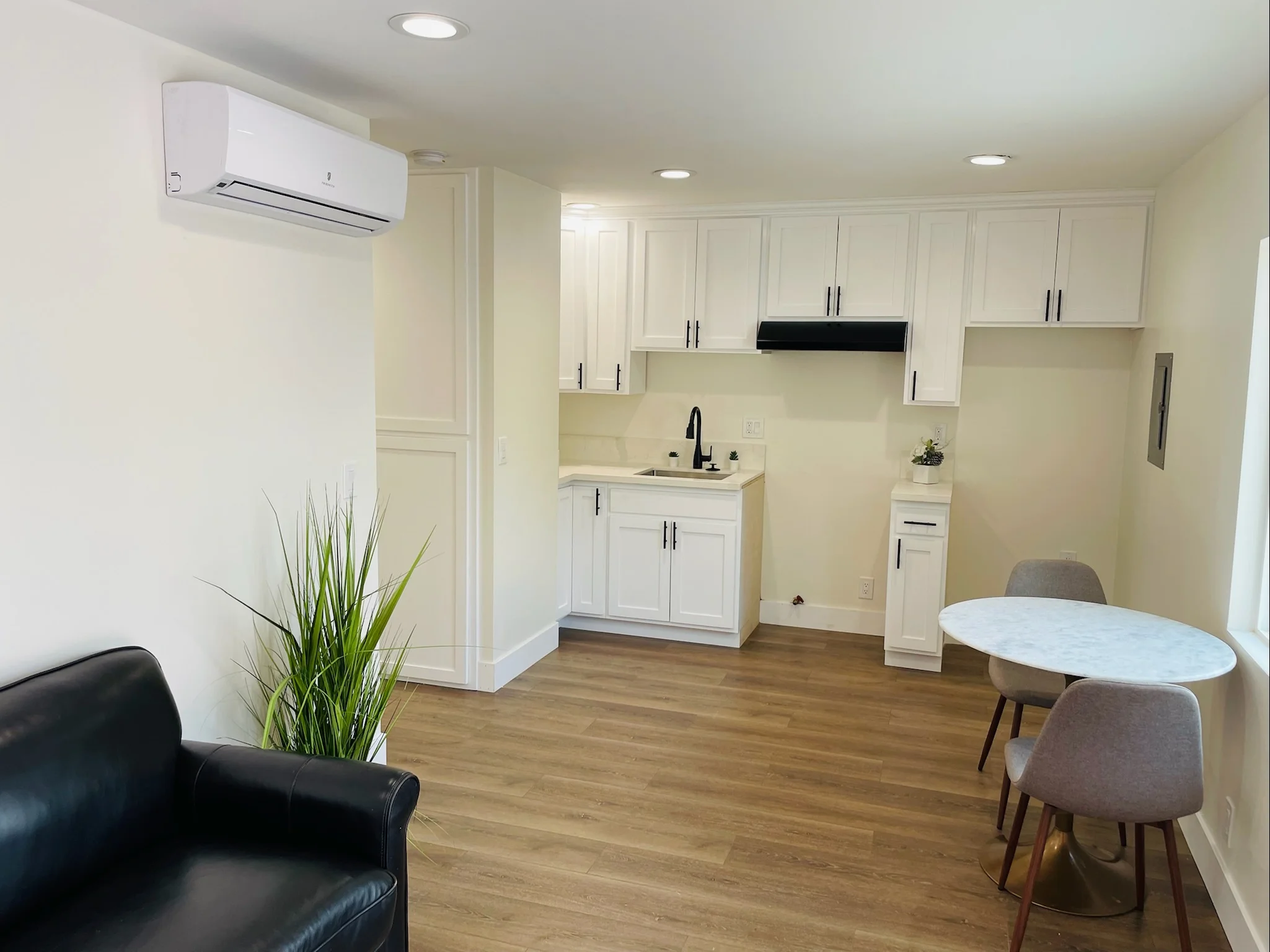 Modern ADU interior with white cabinetry, kitchenette, and dining area on wood flooring