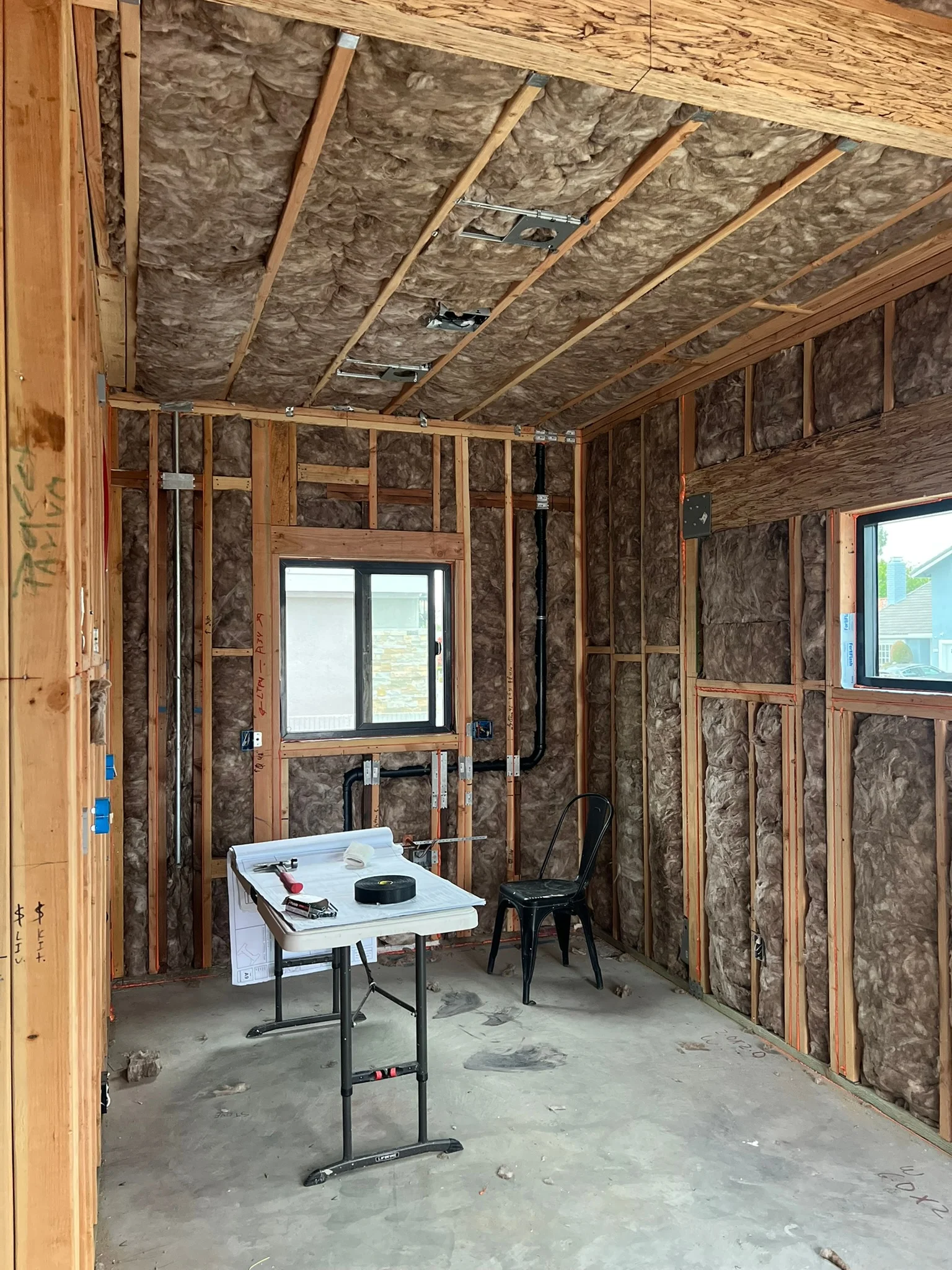 Interior framing with fiberglass insulation, wooden studs, and installed windows during construction phase