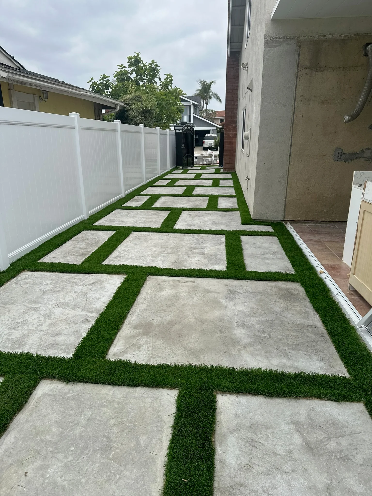 Concrete paver pathway with artificial turf strips and white vinyl fence