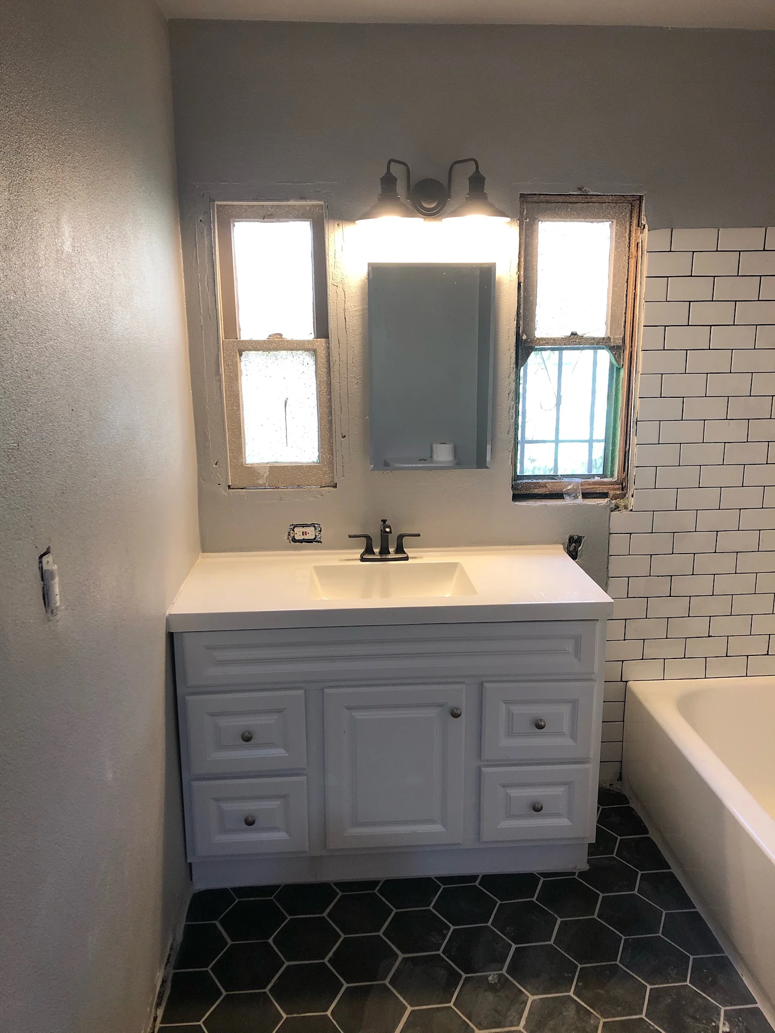 Modern bathroom with gray vanity, white countertop, and black hexagonal floor tiles