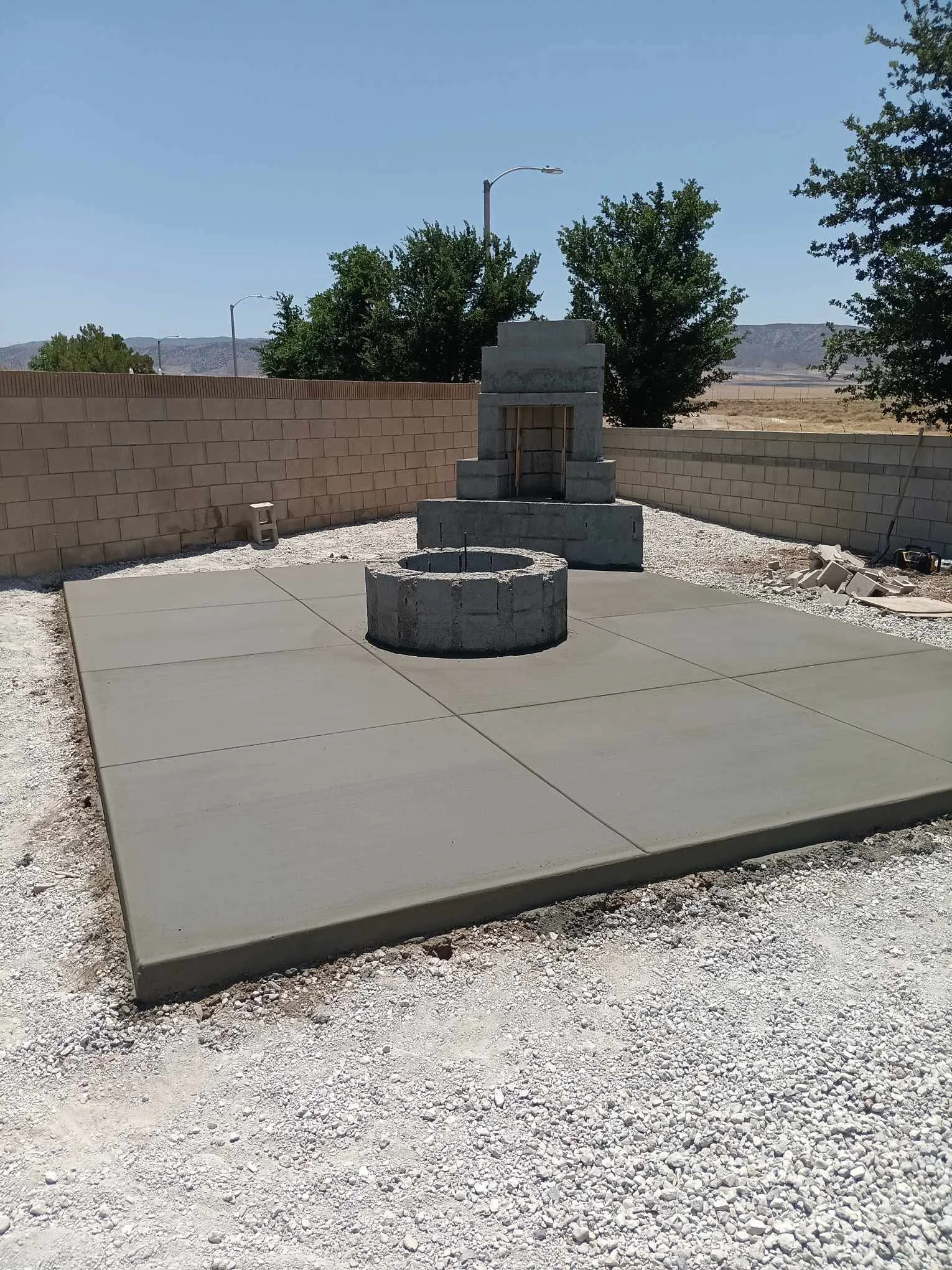 Finished concrete patio with circular fire pit and concrete block walls in residential setting