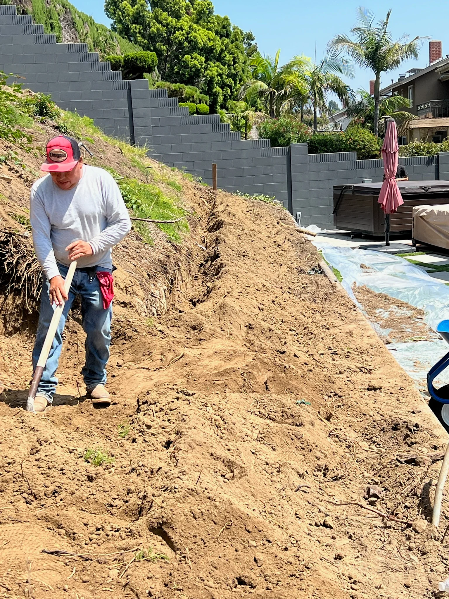 Worker preparing hillside slope with shovel for retaining wall installation