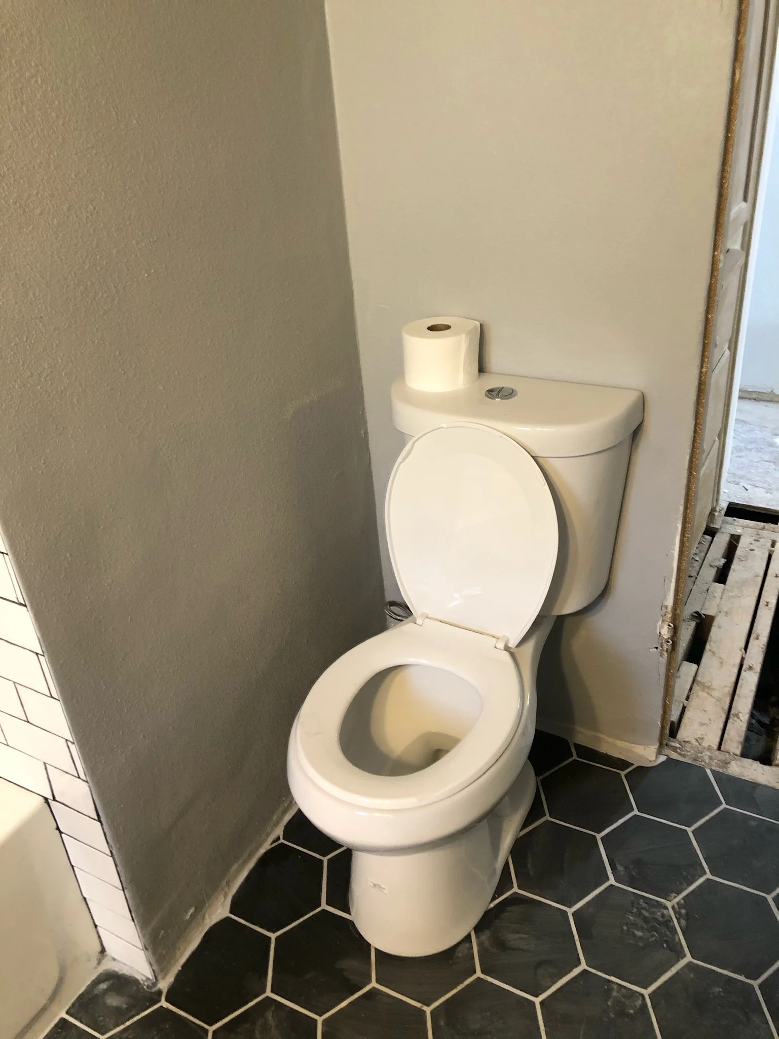 New white ceramic toilet with hexagonal black and white tile flooring in renovated bathroom