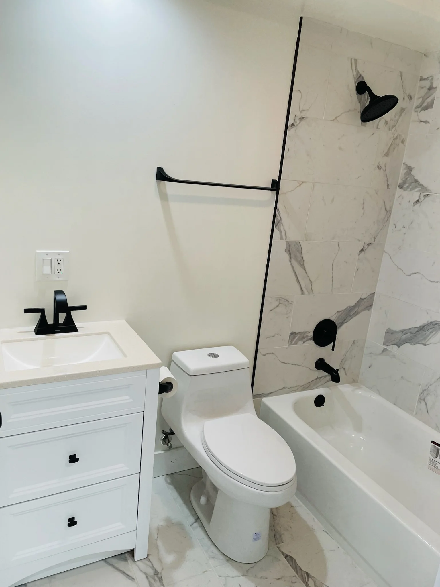 Modern bathroom with marble tile shower, white vanity, and black fixtures
