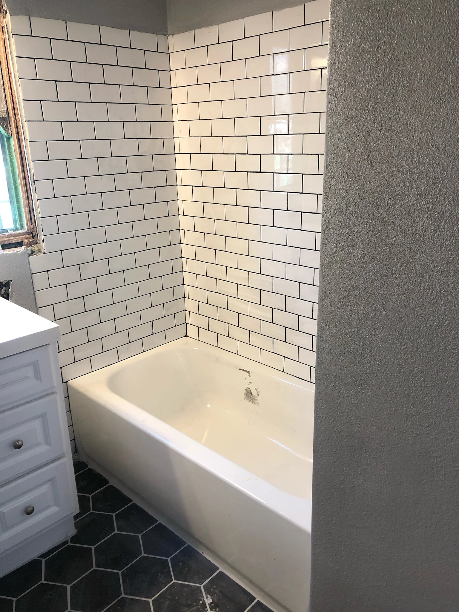 Bathroom with white subway tile walls and black hexagonal floor tile surrounding white soaking tub