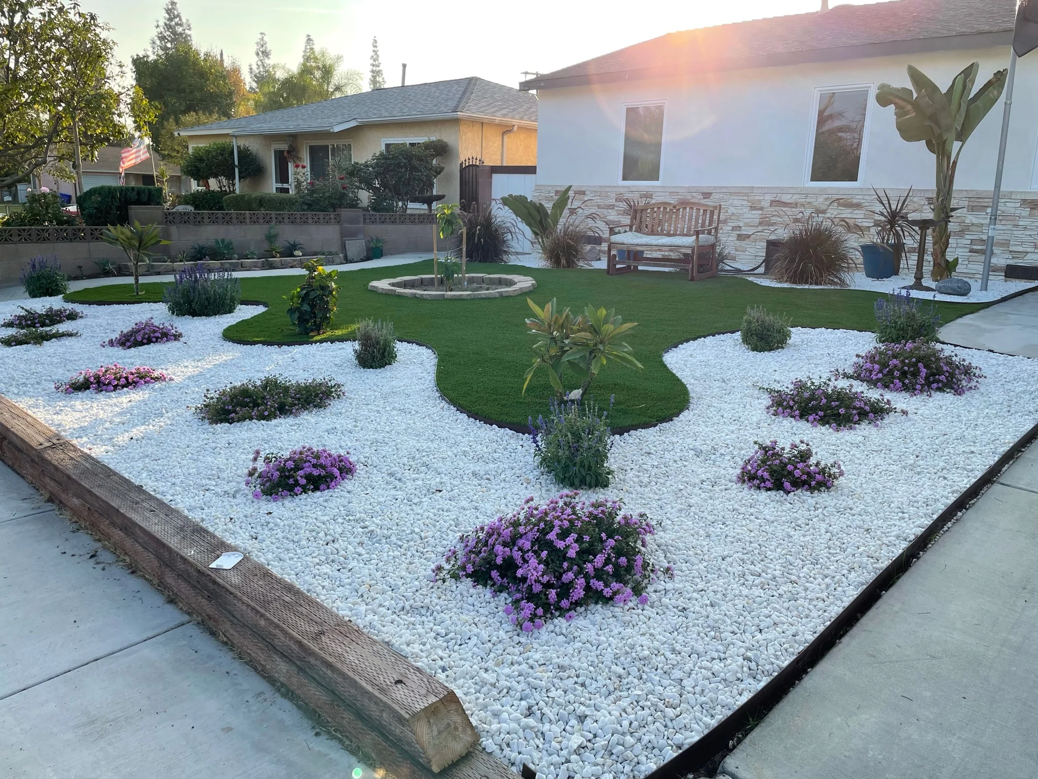 Modern backyard landscape with white rock, purple flowers, artificial turf, and water feature
